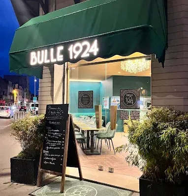 La vitrine éclairée le soir et l'ardoise devant l'entrée de Bulle 1924